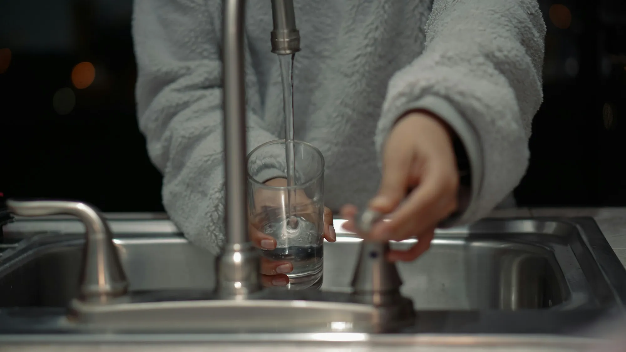 Person filling a drinking glass at a kitchen faucet
