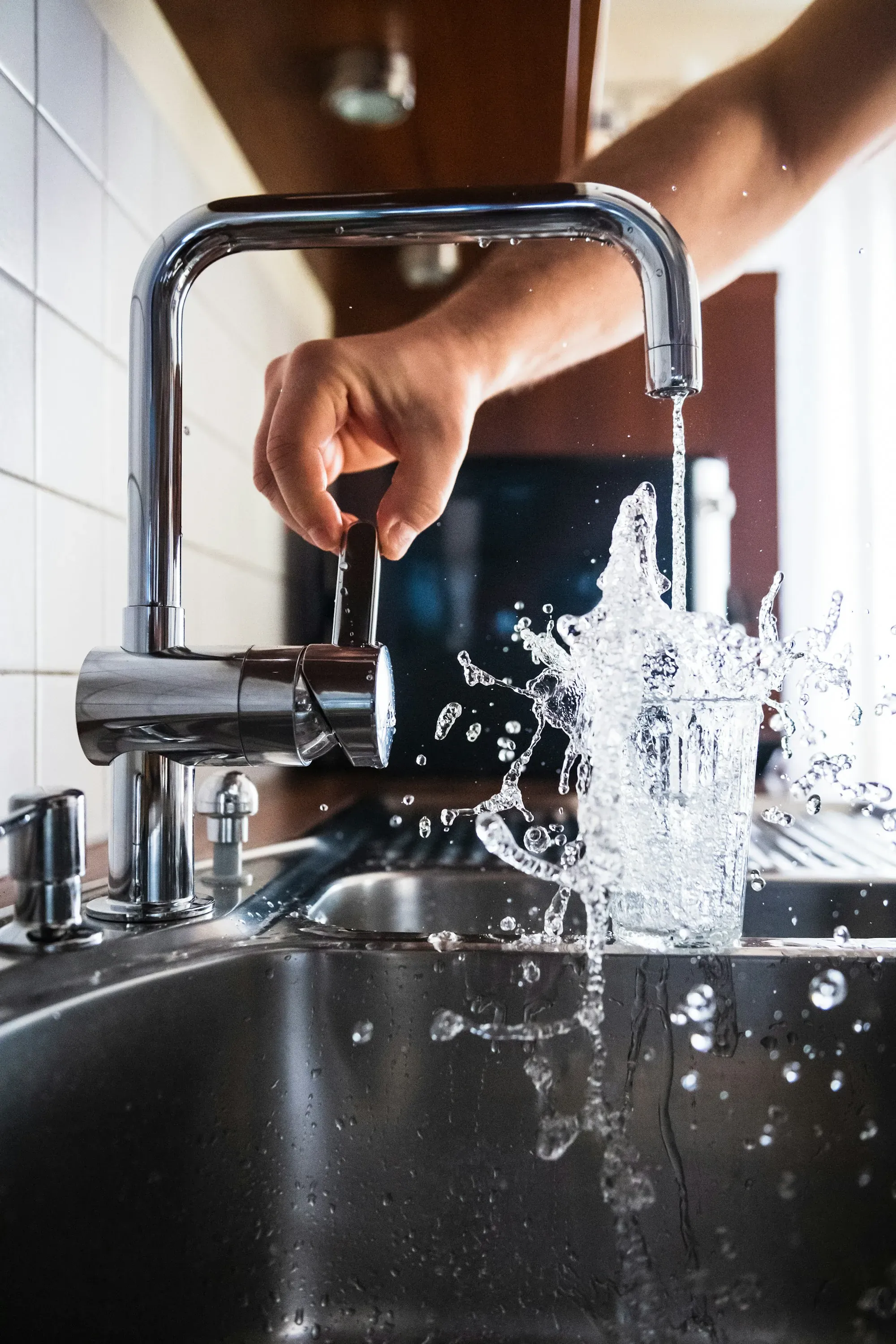 Hand holding a glass under a running kitchen tap